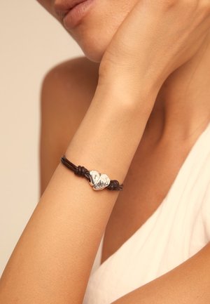 Pulsera de cuero en marrón oscuro con dos acentos de corazón plateados, uno grabado con la palabra "amor". Textura suave, diseño ajustable.