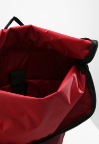 Bolsa impermeable roja con una abertura amplia, cremallera negra y asa integrada. El interior incluye un compartimento para organización.
