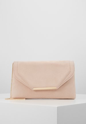 Beige suède clutch met gouden stangdetail op de klep en dunne gouden kettingriem, geplaatst op een wit voetstuk tegen een lichtgrijze achtergrond.