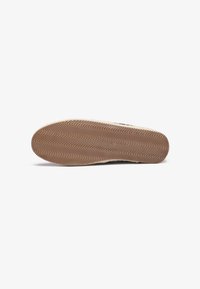 Shoe sole featuring a textured, wavy pattern in light brown rubber, with a reinforced edge for durability and grip.