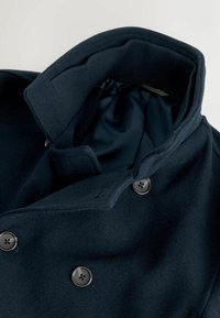 Marineblauer Wollmantel mit großem Kragen, zweireihigem Design und Metallknöpfen. Innenfutter aus glattem Stoff; sichtbare Nähte.