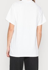 Bílá bavlněná tričko s krátkými rukávy, rovného střihu a klasickým kulatým výstřihem, s jednoduchým zadním dílem a volným střihem.