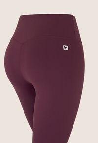Leggings bordeaux con vita alta, realizzati in tessuto elasticizzato. Presentano un piccolo logo vicino alla vita e cuciture piatte per il comfort.