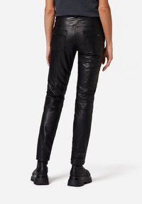 Schwarze Leder-Skinny-Hose mit mehreren Taschen, die eine glatte Textur und ein elegantes Design aufweisen. Das Styling umfasst Nahtdetails und eine figurbetonte Form.