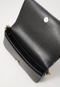 Black textured faux leather crossbody bag with a magnetic snap closure and gold hardware, featuring a single interior compartment.