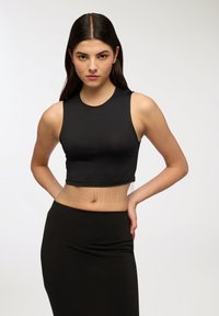 Czarny crop top z gładkiego materiału o wysokim dekolcie i łańcuszkowym zdobieniu na dole. W połączeniu z jednolitą czarną spódnicą.