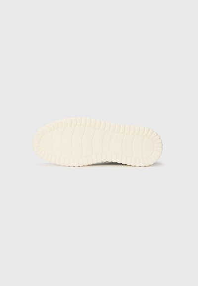 Off-white shoe sole with deep grooves and textured tread pattern, flat on a plain light background.