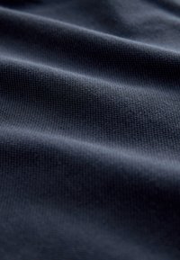 Sötétkék texturált szövet kis szőtt mintával, lágy redőkben és finom megvilágításban bemutatva.