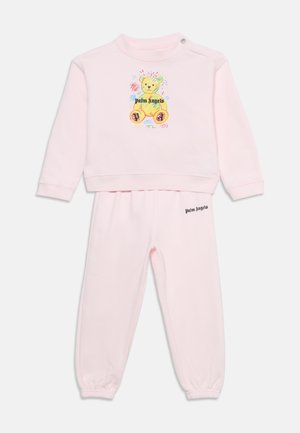 Lichtroze peuter trainingspak met lange mouwen en broek, met een kleurrijke teddybeer en de tekst ""Palm Angels"" op het shirt en de broek.