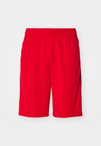 Shorts de sport rouges avec une taille élastique et des panneaux latéraux noirs sur fond blanc.
