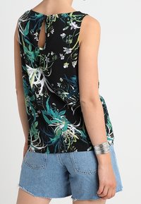 Top senza maniche nero con motivi floreali, caratterizzato da stampe botaniche verdi e bianche, dettaglio sulla schiena a chiave e vestibilità ampia, abbinato a pantaloni shorts in denim.