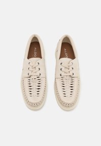 Zapatos beiges de cordones con detalle trenzado en la parte delantera, parte superior de cuero suave y suela de goma. Presentan ojales de tono plateado.