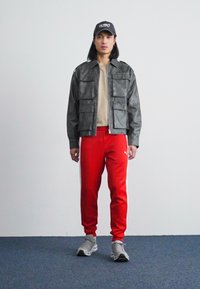 Grå skinnjakke med store lommer, beige t-skjorte, røde joggebukser og grå sneakers. Komplettert med en svart caps.