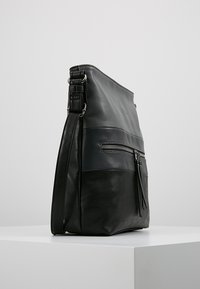 Bolsa de hombro de cuero negro con una textura suave, que cuenta con un bolsillo frontal con cremallera y una correa ajustable para mayor comodidad.