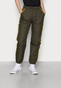 Groene gewatteerde broek met gele zijkanten, een trekkoord in de taille en zijzakken, gecombineerd met witte hoge sneakers.