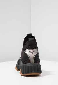 Bakifrån av svarta Puma-sneakers med tjock gummisula och dragflik mot vit bakgrund.