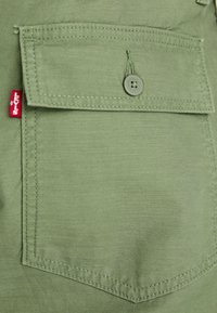 Olive green fabric with a front pocket featuring a button, visible stitching, and a small red Levi's tag attached to the side.