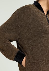 Braune Reißverschlussjacke aus strukturiertem Stoff mit schwarzen Samtbündchen und -kragen. Mit seitlichen Taschen und einer legeren Silhouette.