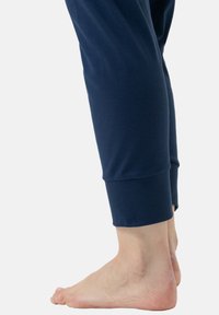 Laivansiniset kevyet juoksuhousut, joissa on tiukka resori nilkassa, sileä pinta ja vartalonmyötäinen malli, yhdistettynä paljaisiin jalkoihin.