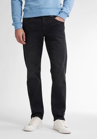 Zwarte denim jeans met een rechte pijp, vijfzakkenontwerp en subtiele vervaging, gecombineerd met witte sneakers en een lichtblauwe sweatshirt.