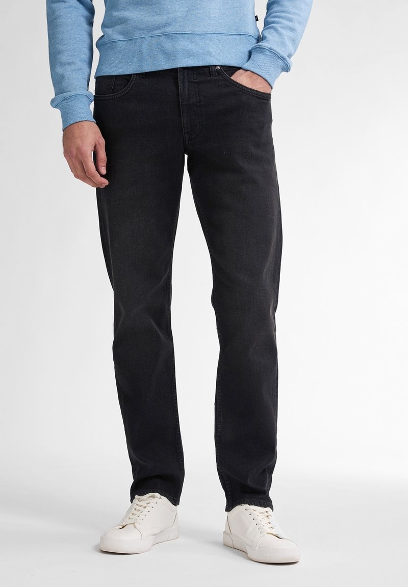 Jeans de denim negro con corte recto, diseño de cinco bolsillos y un ligero desvanecimiento, combinados con zapatillas blancas y un sudadera de color azul claro.