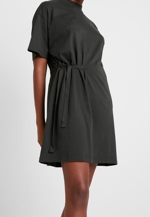 Robe courte noire avec manches courtes et ceinture nouée sur le côté, portée par une personne à la carnation medium-foncée, cadrée aux épaules et au milieu de la cuisse.
