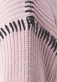 Stickad tröja i mjuk rosa tyg med kontrasterande svarta sömmar och texturerade mönster, som framhäver en mysig och unik design.