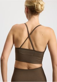 Pruun sooniline sportlik rinnahoidja ristkinnitusega rihmade ja laia elastse paelaga. Sile tekstuur, keha järgnev disain ja minimaalne nähtav riistvara.