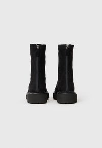 Bottines en suede noir avec une fermeture éclair à l'arrière, semelle plate-forme chunky noire et surpiqûres contrastantes le long des bords.