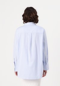 Camisa listrada em azul claro e branco com pregas nas costas, mangas longas e punhos com botão. Material de algodão com um ajuste descontraído.