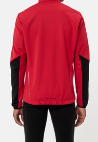 Veste de sport rouge avec manches noires, en matériau lisse et flexible. Dispose d'un col montant, de poches latérales zippées et d'un logo à l'ourlet.