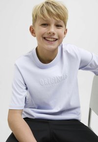 Šviesiai violetinė trumpomis rankovėmis marškinėliai su įspaustu "ORIGINALS" tekstu. Lygus medvilninis audinys, apvalus iškirpimas, derinami su juodomis kelnėmis.