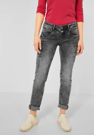 Jeans en denim gris avec un lavage délavé, coupe slim, ourlets roulés et fermeture à boutons. Associés à des baskets crème en tissu texturé.