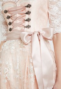 Une robe corset rose avec des manches en dentelle, ornée de lacets en ruban de satin et d'un grand nœud en satin à la taille. Détails décoratifs de perles et de dentelle florale.