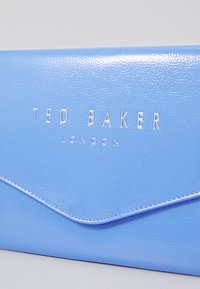 Clutch in ecopelle blu con logo "TED BAKER LONDON" in argento, caratterizzato da una texture liscia e un design a busta con bordi arrotondati.