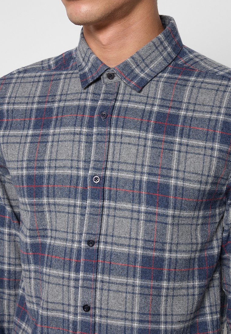 Koszula flanelowa zapinana na guziki w odcieniu szarym z niebiesko-czerwonym wzorem w kratę. Posiada klasyczny kołnierzyk oraz ciemne guziki z przodu. Miękka tekstura.