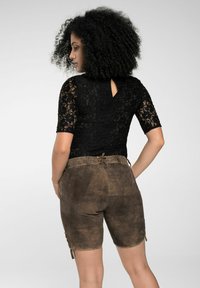 Schwarzes Spitzentop mit kurzen Ärmeln, kombiniert mit braunen Wildleder-Shorts mit seitlichen Schnürdetails und einem Knoten am Bund.