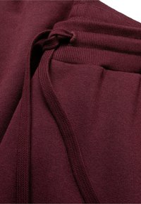 Bordeauxfarbene Sweatpants mit strukturierter Oberfläche, Kordelzug und geripptem Taillenbund, die einen weichen, gestrickten Stoff präsentieren.