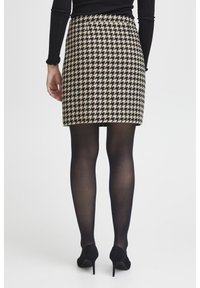 Beżowo-czarna spódniczka mini w wzór houndstooth, zestawiona z czarnymi rajstopami i butami na wysokim obcasie, widok z tyłu.