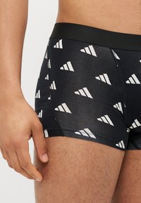 Μαύρα μποξεράκια με λείο υλικό, που διαθέτουν επαναλαμβανόμενο λευκό τριγωνικό σχέδιο και μαύρη ελαστική ζώνη.