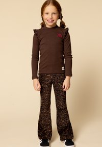 Bruine blouse met lange mouwen en ruches, gecombineerd met flared broek met luipaardprint in bruin en zwart. Model draagt zwarte sneakers.