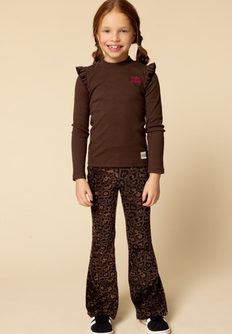 Bruine blouse met lange mouwen en ruches, gecombineerd met flared broek met luipaardprint in bruin en zwart. Model draagt zwarte sneakers.