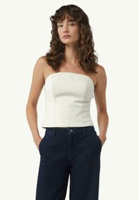 Biała bluzka bez ramiączek o ustrukturalizowanym fasonie i widocznych szwach, zestawiona z ciemnoniebieskimi spodniami o wysokim stanie. Gładki materiał i dopasowany krój.