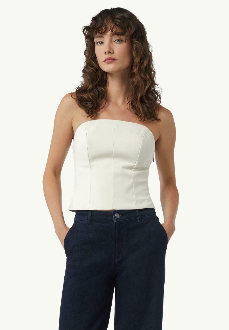 Biała bluzka bez ramiączek o ustrukturalizowanym fasonie i widocznych szwach, zestawiona z ciemnoniebieskimi spodniami o wysokim stanie. Gładki materiał i dopasowany krój.