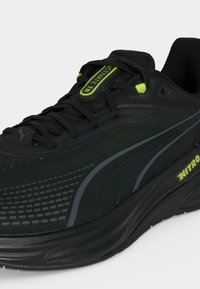 Μαύρο αθλητικό παπούτσι με γκρι λογότυπο Puma, lime πράσινες λεπτομέρειες, κορδόνια και το κείμενο "NITRO" στη σόλα, εμφανιζόμενο από μπροστινή πλευρική γωνία.