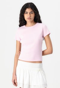 Pink fitted t-shirt with short sleeves and a round neckline, made from a smooth fabric, paired with a white ruffled skirt.