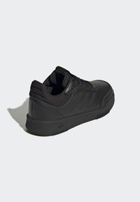 Baskets de sport noires avec une tige synthétique lisse, des accents texturés, des lacets plats et une semelle en caoutchouc flexible. Présente trois bandes sur le côté.