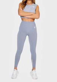 Jasnoszary sportowy crop top i legginsy o wysokim stanie o gładkiej fakturze, z białymi akcentami logo i detalami przeszyć.