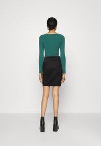 Grön figurnära långärmad topp, svart hög midja kjol och svarta klackade ankelstövlar. Slät textur, elegant design och minimalistisk stil.