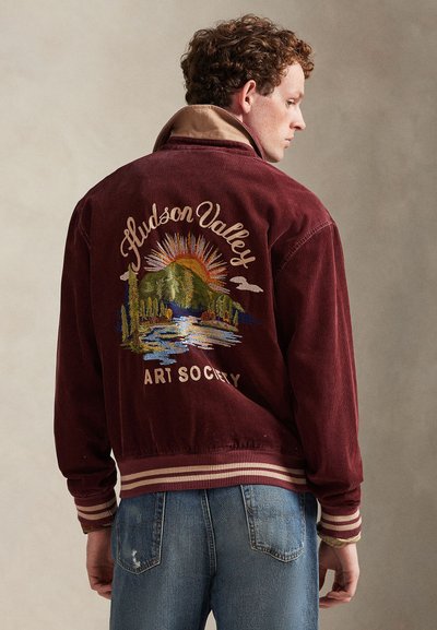 Bordeaux rode ribfluwelen jas met een beige kraag, met een geborduurd landschap en de tekst "Hudson Valley Art Society" op de achterkant.